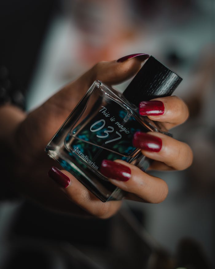 Close-up of a female hand with manicured nails holding a luxurious perfume bottle.
